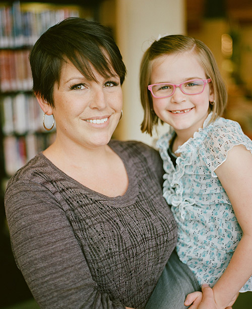 Adult woman with short brown hair holding child and smiling at camera.
