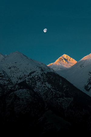 Evening sky with snowy mountains and moon.